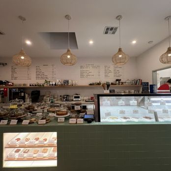 Gati - The image shows the interior of a bakery or ice cream shop with a green tiled counter displaying baked goods and ice cream flavors. Pendant lights hang from the ceiling, and a menu is visible on the wall behind the counter. The space includes equipment and shelves with various items, creating a cozy and modern atmosphere. - Ice Cream & Frozen Yogurt Near Me - Austin, Texas