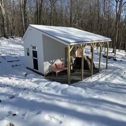 JM Sheds - Shed exterior from uphill, with overhang. Top of 3' high rock wall sort of visible, covered with snow.