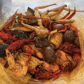Cap't Loui - A seafood boil includes various shellfish such as shrimp, crab, mussels, and potatoes, along with corn on the cob, all coated in a spicy sauce. The dish is served in a large, transparent container lined with plastic, placed on a white surface, with some drinks visible in the background. The presentation emphasizes a communal, seafood-focused dining experience. - Cajun/Creole Near Me - Providence, Rhode Island