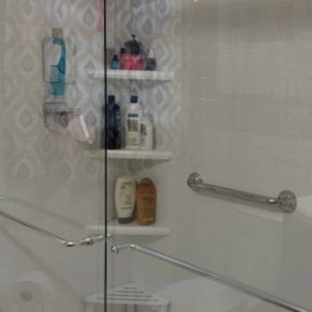 DaBella - Clear shower door I didn't order - A shower area with a glass door, featuring built-in shelves stocked with shampoo, soap, and other toiletries. - Roofing Near Me - Redding, California