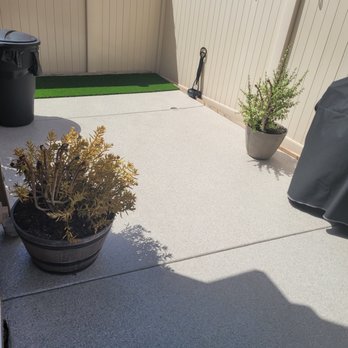 Epoxy Time - A backyard patio features two potted plants, a trash bin, string lights on a beige fence, and a small green mat. - Flooring Near Me - Riverside, California