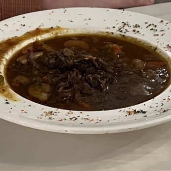 Highfields Restaurant & Eagle Landing Tavern - Pot Roast - A bowl of pot roast with dark gravy, vegetables, and shredded meat, served on a white plate with herbs around the edge. - New American Near Me - Jackson, New Hampshire