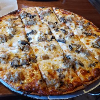 The Ding - Mushroom and sausage pizza - A large mushroom and sausage pizza with melted cheese, cut into slices, on a wooden table at a restaurant. - Bars Near Me - Wild Rose, Wisconsin