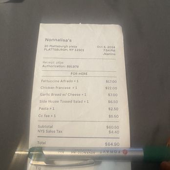 Nonna Lisas Kitchen - $5.50 charge for using a credit card!!!! Are these people insane?????? - A printed receipt from Nonnalisa's restaurant located at 20 Plattsburgh Plaza, Plattsburgh, NY, dated October 4, 2024, at 7:54 PM. The receipt lists food items including fettuccine Alfredo, chicken francese, garlic bread with cheese, side house tossed salad, pasta, and coffee, along with their prices. A pen is placed at the bottom of the receipt, partially covering it. The background appears to be a dark surface, possibly a table or counter. - Italian Near Me - Plattsburgh, New York