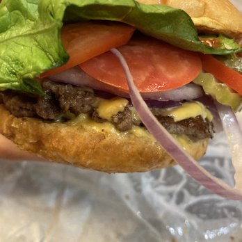 Smashburger - a hand holding a hamburger with lettuce, tomato, and onion - Burgers Near Me - Fargo, North Dakota