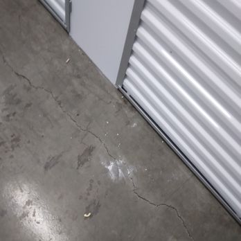 Extra Space Storage - The image shows a concrete floor with multiple visible cracks and some scattered debris, including small pieces of trash. Next to the floor is a metal storage unit with corrugated panels, likely part of a storage facility or warehouse. The setting appears industrial or utilitarian, with no other objects or people present. - Self Storage Near Me - Berwyn, Illinois