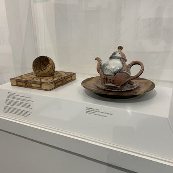 Fuller Craft Museum - Ceramic art pieces, including a teapot with a plate and a small bowl, are displayed in a museum case with informational labels. - Museums Near Me - Brockton, Massachusetts