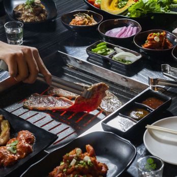 Woomeeok Korean BBQ & Hot Pot - a person preparing food on a grill - Korean Near Me - Plano, Texas Woomeeok Korean BBQ & Hot Pot - a person preparing food on a grill - Korean Near Me - Plano, Texas
