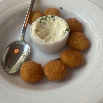 Blu - Tater tots - Fried croquettes arranged around a small cup of creamy dipping sauce on a white plate, with a spoon resting on the side. - French Near Me - Glen Arbor, Michigan