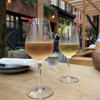 Runner Up - Rosé and white wine by the glass - Two wine glasses, one with rosé and one with white wine, are placed on a wooden table in an outdoor dining setting with a brick building and wooden pergola. - French Near Me - Brooklyn, New York