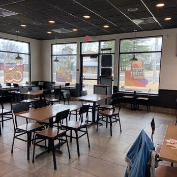 Taco Bell - Clean lobby.  Due to respect, I waited for all 3 groups of guests to leave so they wouldn't be in picture. - The image depicts the interior of a Taco Bell restaurant with several unoccupied tables and chairs arranged throughout the dining area. Large windows allow natural light to enter, with promotional decals on the glass. The ceiling is black with recessed lighting, and a wall-mounted TV is visible on the right side. The space appears clean and organized, with some items on a table in the foreground. - Tacos Near Me - Cuba, Missouri