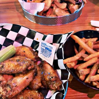 King Jugg Brewing - A meal setup includes a basket of seasoned chicken wings, a bowl of French fries, and a tray of fried chicken, all on a wooden table at a restaurant. - Brewpubs Near Me - Fishers, Indiana
