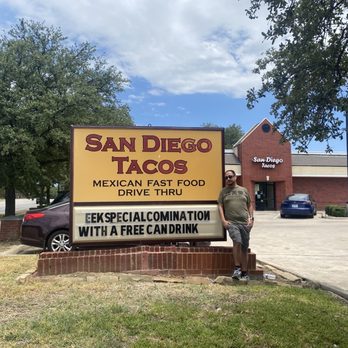 San Diego Tacos Shop - Husband posing with sign. - Mexican Near Me - Irving, Texas