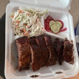 Spicy Pickled Onion Slices - A takeout container holds smoked barbecue ribs, coleslaw, and pickles, served in a casual dining setting.