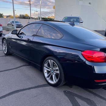 Precision Cut Window Tint - Ceramic Tint - A black BMW coupe with tinted windows is parked in a lot near a white building, with other cars and a partly cloudy sky in the background. - Car Window Tinting Near Me - Tempe, Arizona