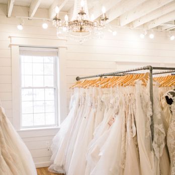 Cleo Bridal - Wedding dresses hanging on wooden hangers in room with white walls and chandelier. - Bridal Near Me - O'Fallon, Missouri Cleo Bridal - Wedding dresses hanging on wooden hangers in room with white walls and chandelier. - Bridal Near Me - O'Fallon, Missouri