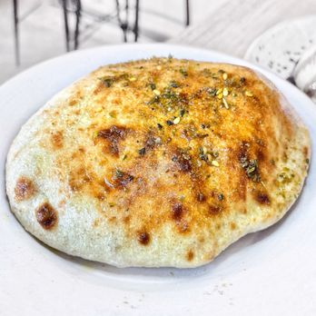 Azhar - A piece of naan bread with herbs and sesame seeds on top, served on a white plate, likely in a restaurant setting. - Middle Eastern Near Me - Toronto, Ontario