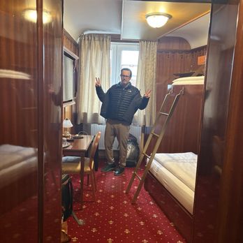 Hotel du Train - My silly spouse inside our bunk room. There's a mini fridge, safe, closets with hangers, a desk, and a TV with German channels - Hotels Near Me - Munich, BY