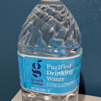 Target - $1.39 - A clear plastic bottle containing purified drinking water, with a white handle attached to the cap for easy carrying. The bottle has a blue label indicating it is purified water, processed with advanced filtration and reverse osmosis technology. The bottle is positioned on a white surface with a textured blue wall in the background. - Department Stores Near Me - Tucson, Arizona