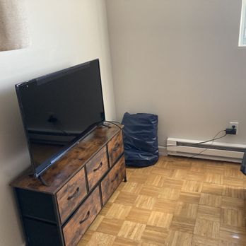 A O Construction - TV stand/ dresser - A bedroom corner features a flat-screen TV on a wooden dresser, a window, and a bag on the floor near the wall. - Excavation Services Near Me