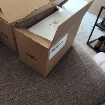 Xfinity Store by Comcast - A cardboard box with the Xfinity logo is open, revealing a white package inside, on a textured brown surface. - Internet Service Providers Near Me - Albuquerque, New Mexico