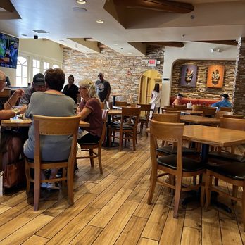 Thunderbird Bar & Grill - A restaurant interior featuring wooden tables and chairs, with a brick wall and artwork, and patrons dining at various tables. - American Near Me - Santa Fe, New Mexico