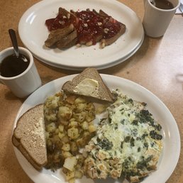 Stuffed French Toast (cream cheese, walnuts and strawberries ) The Chelsea Boy (grilled chicken, spinach and egg whites) - A breakfast meal with two plates: one with French toast topped with strawberries and syrup, and another with scrambled eggs, hash browns, and toast, accompanied by two cups of coffee.