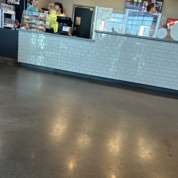Elevate Trampoline Park - Food counter.  Nachos, fries, pizza, etc. - A fast-food restaurant counter with employees, a digital menu display, and a glass partition, featuring a Coca-Cola vending machine. - Trampoline Parks Near Me - Queen Creek, Arizona
