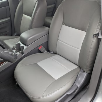 Cibola Upholstery - The image depicts the front passenger seat of a vehicle with leather upholstery in gray and light gray tones. The seat has a contoured design with visible stitching and a headrest. The center console with cup holders and a gear shift is visible, along with part of the driver's seat and the vehicle's interior door panel. The interior appears clean and well-maintained. - Furniture Reupholstery Near Me - Corrales, New Mexico