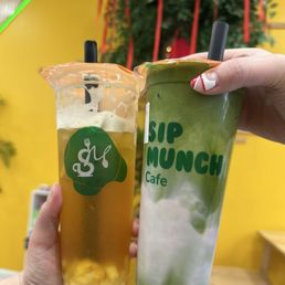 Two beverages from Sip Munch Cafe are shown, one with a green tea appearance and the other with a yellowish hue, held by two different hands.