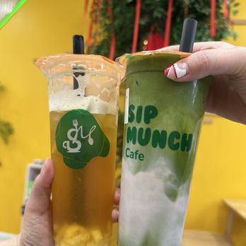 Sip Munch Cafe - Two beverages from Sip Munch Cafe are shown, one with a green tea appearance and the other with a yellowish hue, held by two different hands. - Coffee & Tea Near Me - Austin, Texas