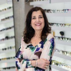 Specs & Spines Optometry and Chiropractic - Rosanna standing in front of a wall of eyeglasses inside Specs & Spines Optometry in Toronto.