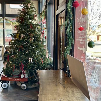 Sugarlump - A Christmas tree decorated with ribbons and ornaments is placed inside a shop near large windows, with a wagon of gifts at its base. - Coffee & Tea Near Me - Westcliffe, Colorado