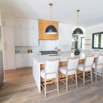 Infinity Custom Cabinets - Bright and airy modern kitchen featuring sleek white cabinetry, with white oak accents, a stainless steel gas range, and a large island. - Cabinetry Near Me - Leland, North Carolina