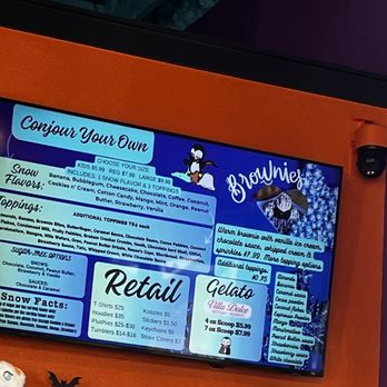 Vampire Penguin - See menu under "conjure your own" - A digital menu board at Vampire Penguin ice cream shop shows flavors, toppings, and retail items, with colorful graphics and text. - Shaved Snow Near Me - Hurst, Texas