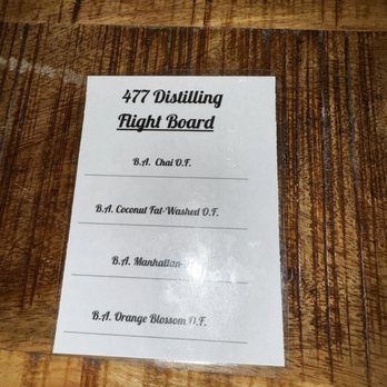 477 distilling  - Flight - A flight board menu from 477 Distilling lists four different cocktails or spirits on a wooden surface. - Distilleries Near Me - Greeley, Colorado
