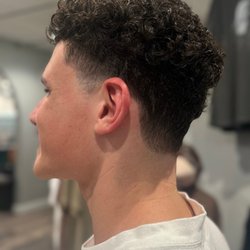 Pin-Up Curls - Fresh men's curly haircut with a clean taper and natural texture on top. Men's hair services at Pin-Up Curls in Fort Wayne.