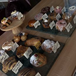 Pastries - A glass display case contains various pastries such as croissants, donuts, and éclairs, each labeled with handwritten tags, in a bakery setting.