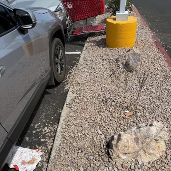 Target - A red shopping cart is tipped over and leaning against a silver car in a parking lot, with other vehicles visible in the background. - Department Stores Near Me - Mesa, Arizona