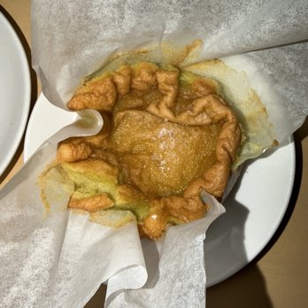 Baleia - Olive oil cake - A fried pastry with a golden-brown, crispy exterior is placed on a white plate, partially wrapped in parchment paper. - Wine Bars Near Me - Boston, Massachusetts