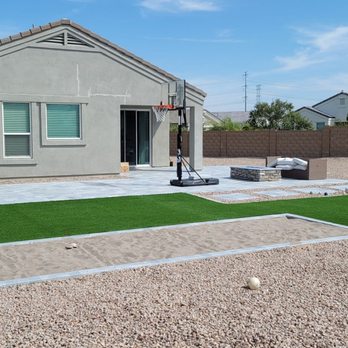 TheHardworkers - A backyard features artificial grass, gravel, a patio with a basketball hoop, and outdoor seating, with neighboring houses in the background. - Landscape Architects or Designers Near Me - Mesa, Arizona