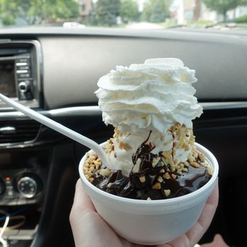 Dairy Belle - Brownie Sundae to go - A bowl of ice cream topped with whipped cream, chocolate syrup, and nuts is held inside a vehicle, with the car's dashboard and windshield visible. - Ice Cream & Frozen Yogurt Near Me - Hammond, Indiana