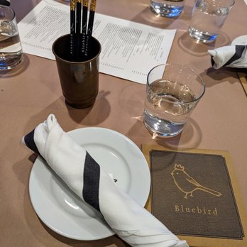 Bluebird - Inside. Table setting. Pencils are used to draw on the paper covering the table. Menu unfolds. - French Near Me - Chapel Hill, North Carolina