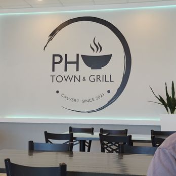 Pho Town - Such a clean restaurant! Spotless, every time I come - Inside Pho Town & Grill, a wall displays the restaurant's logo with a steaming bowl graphic, and there are several black dining tables and chairs. - Vietnamese Near Me - Prince Frederick, Maryland