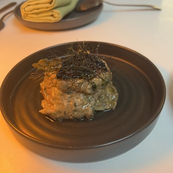 Taline - Babaghanoush - A serving of baba ghanoush, a Middle Eastern eggplant dip, garnished with black herbs, presented on a black plate. - Mediterranean Near Me - Toronto, Ontario