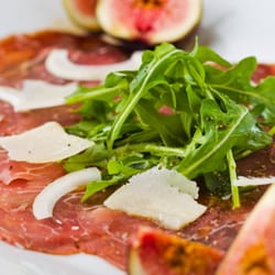 L'Escapade Gourmande - Carpaccio de bœuf aux copeaux de parmesan et à la roquette, assaisonné d'un filet d'huile d'olive, et décoré avec des figues.
