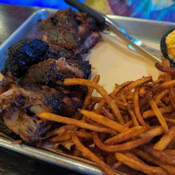 A close-up shot of smoked meat and sweet potato fries on a metal tray.