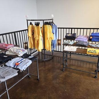Avery Brewing - Merch - Various clothing items, including t-shirts and sweatshirts, are arranged on tables and a clothing rack inside a retail store. - Breweries Near Me - Boulder, Colorado