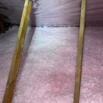Super Green Insulation - The image shows pink cellulose insulation covering the attic floor, with two vertical wooden support beams. The ceiling is lined with reflective foil insulation, which is secured to the rafters. The setup appears to be part of an insulation installation process, aimed at improving energy efficiency and indoor air quality. - Insulation Installation Near Me - Austin, Texas