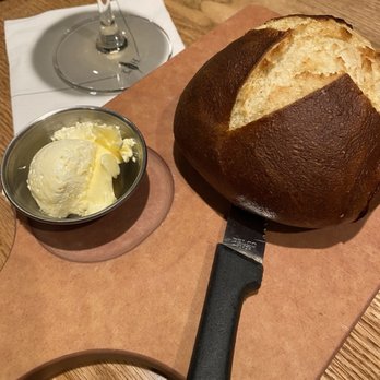 Cooper’s Hawk Winery & Restaurant - A round loaf of bread with a dark crust and soft interior, a butter dish with butter, and a wine glass on a wooden table. - Wine Bars Near Me - Plainfield, Illinois